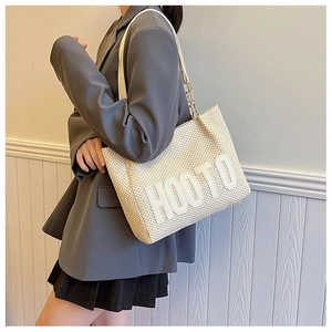Detail of a beige woven tote bag featuring 3D embossed HOOTO lettering and metal chain strap