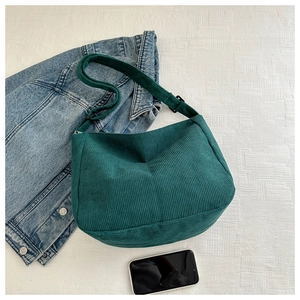 Flat lay of deep green corduroy crossbody bag with adjustable strap and denim jacket