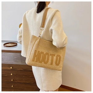 Detail of straw tote bag with HOOTO leather logo and metallic chain strap attachments