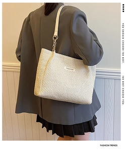 Detail of cream woven tote bag with chain strap and fashion label on street style model