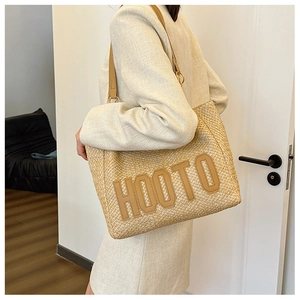 Detail of woven straw tote bag with HOOTO leather lettering and brown shoulder straps