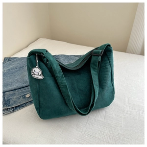 Detail of dark green corduroy tote bag with wide strap and cartoon dog charm accessory