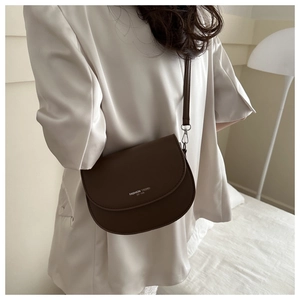 Détail d'un sac besace marron foncé en cuir mat avec lettrage blanc et bandoulière fine