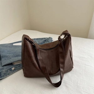 Minimalist large brown leather tote bag on white background with blue denim jacket