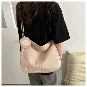 Detail of beige corduroy tote bag featuring a round coin purse charm and vertical texture