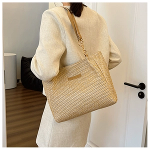Detail of beige straw tote bag featuring woven texture and brown leather fashion patch