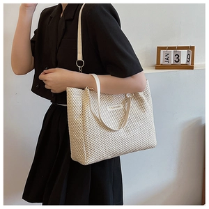 Detailed close-up of a cream woven tote bag featuring a Fashion metal logo and sleek handles
