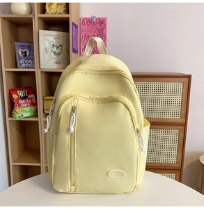 Detail eines hellgelben Nylon-Rucksacks mit modischem Logo und robusten Reißverschlusstaschen