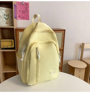 Detailansicht des cremegelben Nylon-Rucksacks mit Seitentaschen und Mode-Etikett