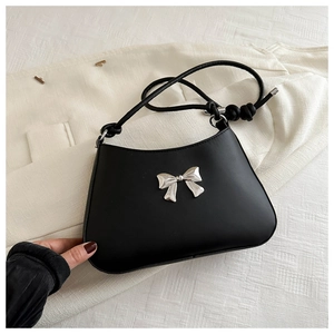 Detailed view of black underarm bag featuring a silver metal bow and knotted shoulder strap