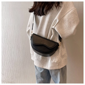 On-body view of a black matte leather saddle bag with a wavy flap and gold buckle detail