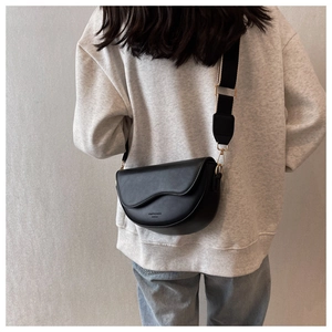 Detailed back view of a black saddle bag featuring a wide fabric strap and gold hardware