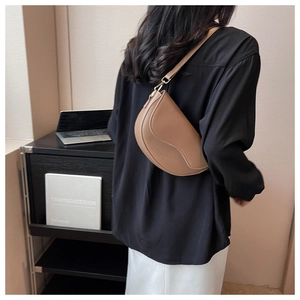 Caramel saddle bag shown as crossbody on model with black shirt and white pants