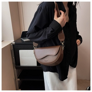 Detail of dark brown leather saddle bag with wide strap and gold hardware on model