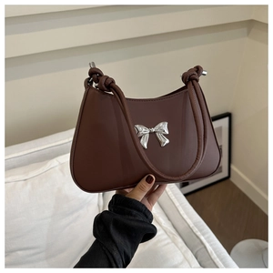 Detail of a brown leather crescent bag with a silver bow ornament and knotted strap