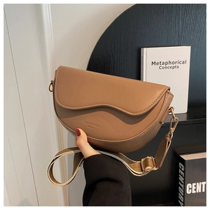 Detail of tan saddle crossbody bag featuring a wavy flap design and wide fabric strap