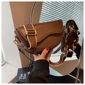 Detail of dark brown saddle bag featuring wide fabric strap and golden hardware