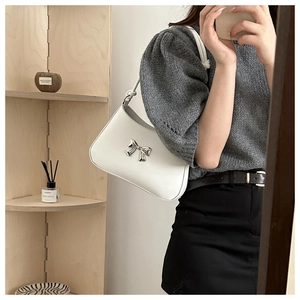Close-up of a white underarm bag with a silver metallic bow detail worn by a model