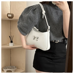 Detailed close-up of a white leather shoulder bag featuring a silver metal bow accent