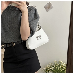 Close-up of a white leather underarm bag featuring a silver bow buckle and sleek design