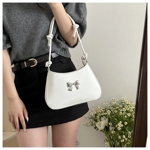 Close-up of a white shoulder bag with a silver metal bow detail on smooth PU leather