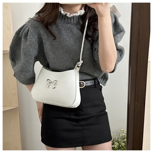 Close-up of a white leather handbag featuring a stylish silver metal bow decoration