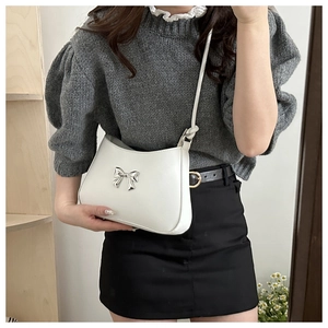 Close-up of a white bow shoulder bag on a model featuring silver metallic hardware detail