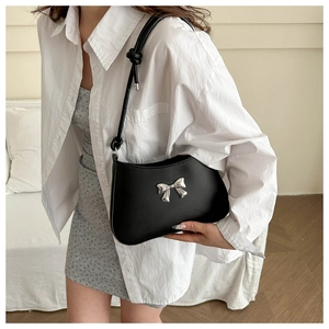 Detail of a black underarm bag featuring a metallic silver bow accent and knotted strap