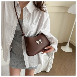 Close-up of a deep brown faux leather shoulder bag with a silver metal bow detail