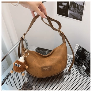 Detail of brown PU crescent bag featuring a monster plush charm and gold zipper