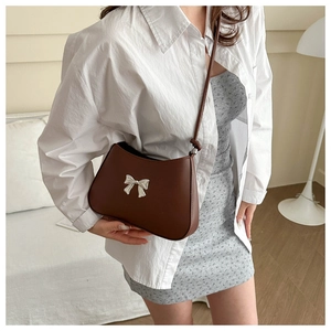 Detail of a brown leather shoulder bag featuring a silver metal bow on a crescent body
