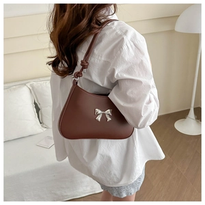 Close-up of brown matte leather shoulder bag with a silver metal bow and knotted strap