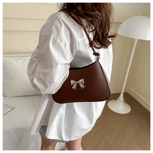 Detail of dark brown leather crossbody bag featuring silver metallic bow and knotted strap
