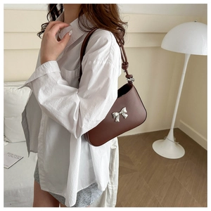 Detail of a dark brown underarm bag with a silver bow ornament and knotted strap detail
