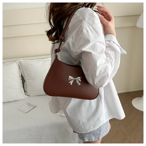 Detail of a brown leather shoulder bag with silver bow accent and knot handle design