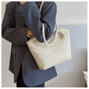 Detail of cream straw tote bag with delicate floral embroidery and tassel charm