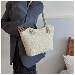 Detail of woven straw tote bag featuring delicate floral embroidery and rope handles