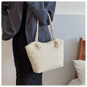 Detail of straw woven tote bag featuring floral embroidery and thick rope handles