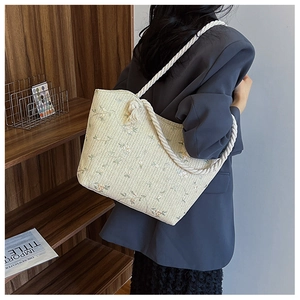 Close-up of woven straw tote bag featuring colorful floral patterns and white rope handles