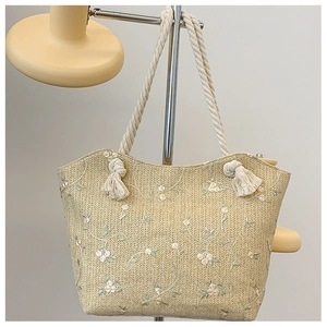 Detail of beige straw tote bag featuring floral embroidery and cotton rope handle