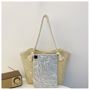 Detail of beige straw tote bag featuring white floral embroidery and woven rope straps