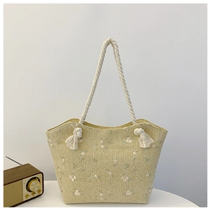 Detail of straw tote bag featuring white floral embroidery and cotton rope handles