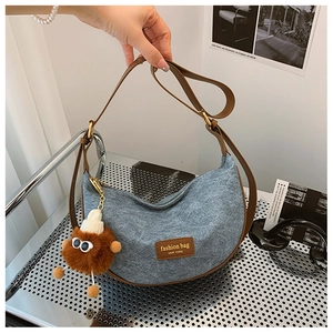 Detail of denim hobo bag with brown leather trim and a cute plush monster charm