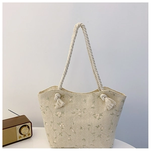 Detail of floral embroidery and cotton rope handle on this beige woven straw tote bag