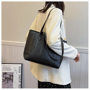 Détail d'un sac cabas noir avec texture ondulée verticale et longues lanières en cuir