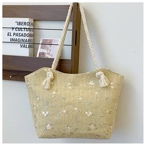 Detailed close-up of straw tote bag featuring white floral lace embroidery and tassels
