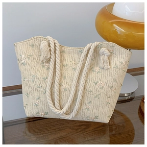 Detailed close-up of straw tote bag featuring floral embroidery and knotted rope handles