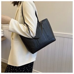 Détail d'un sac cabas noir à texture ondulée porté à l'épaule sur un mur blanc