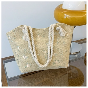 Detail of straw tote bag featuring floral embroidery, cotton rope handles and tassels