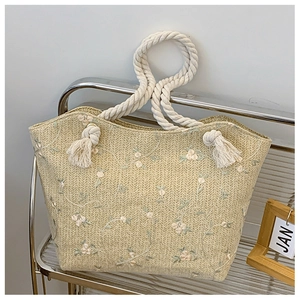 Detail of straw woven tote bag featuring floral embroidery and white rope handle